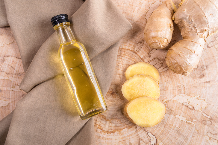 Small Glass Bottle Of Ginger Oil On Brown Cloth And Fresh Ginger On Wooden Saw Cut.